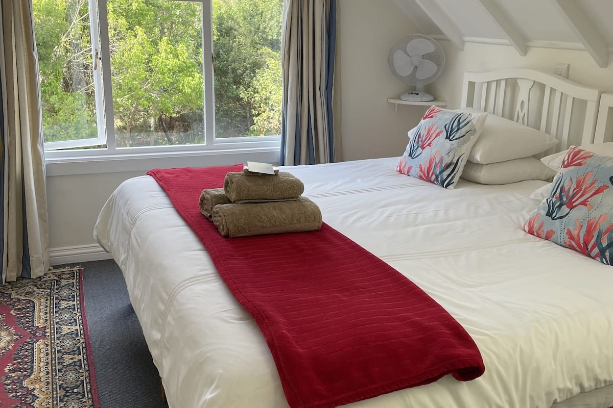 A bedroom with a large bed, a red blanket, a patterned pillow, and a view of trees through a window.