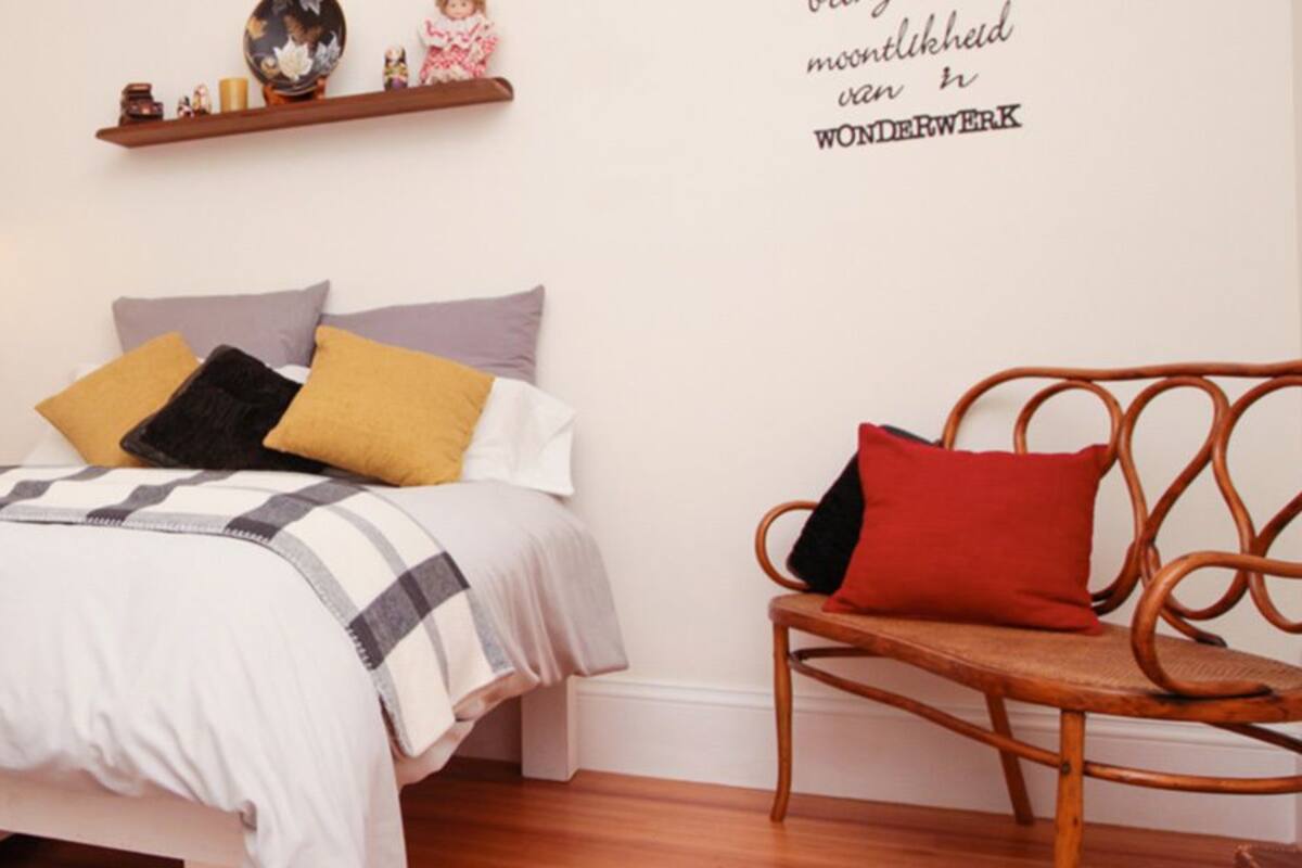A bedroom with a bed, dresser, chair, and a wall with a shelf.