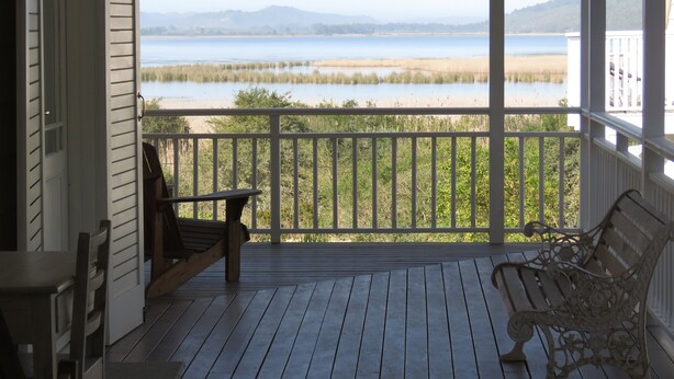 Une terrasse en bois avec deux chaises et une table, d’où l’on peut admirer un lac et, au loin, une chaîne de montagnes.