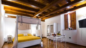 Une chambre à coucher avec un lit à baldaquin, une petite table avec des chaises, un miroir et un téléviseur fixé au mur.