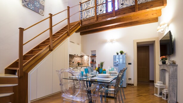 Un espace repas avec un escalier en bois, des chaises transparentes et une cuisine en arrière-plan.