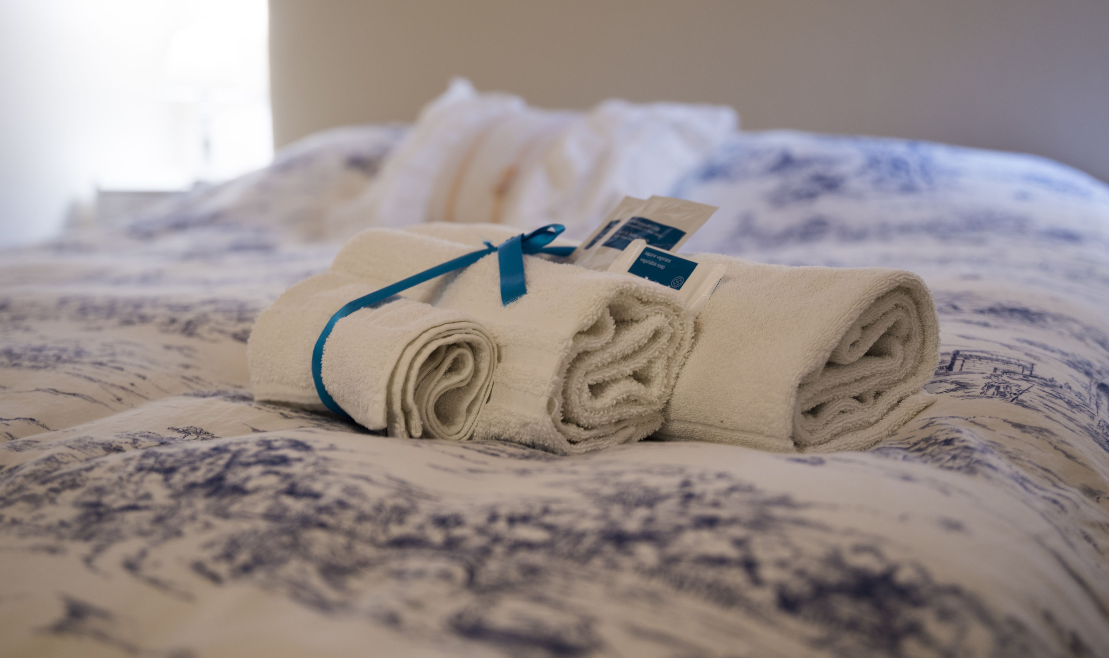 A neatly folded towel with a blue ribbon tied around it, placed on a bed with a patterned bedspread.