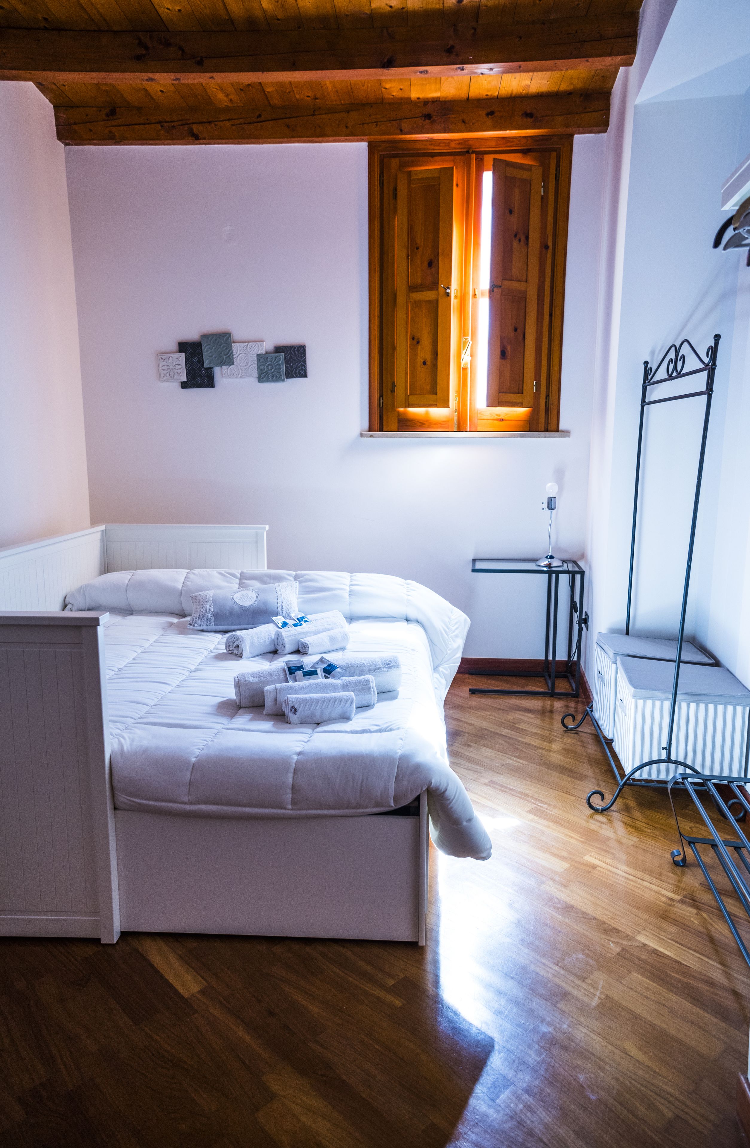 A bedroom with a wooden ceiling, a bed with white bedding, a radiator, and a window with wooden shutters.