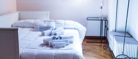 A bedroom with a wooden ceiling, a bed with white bedding, a radiator, and a window with wooden shutters.