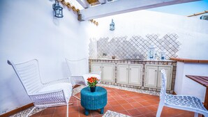 Une terrasse avec des chaises en osier blanc, un pouf bleu tissé et un sol carrelé.