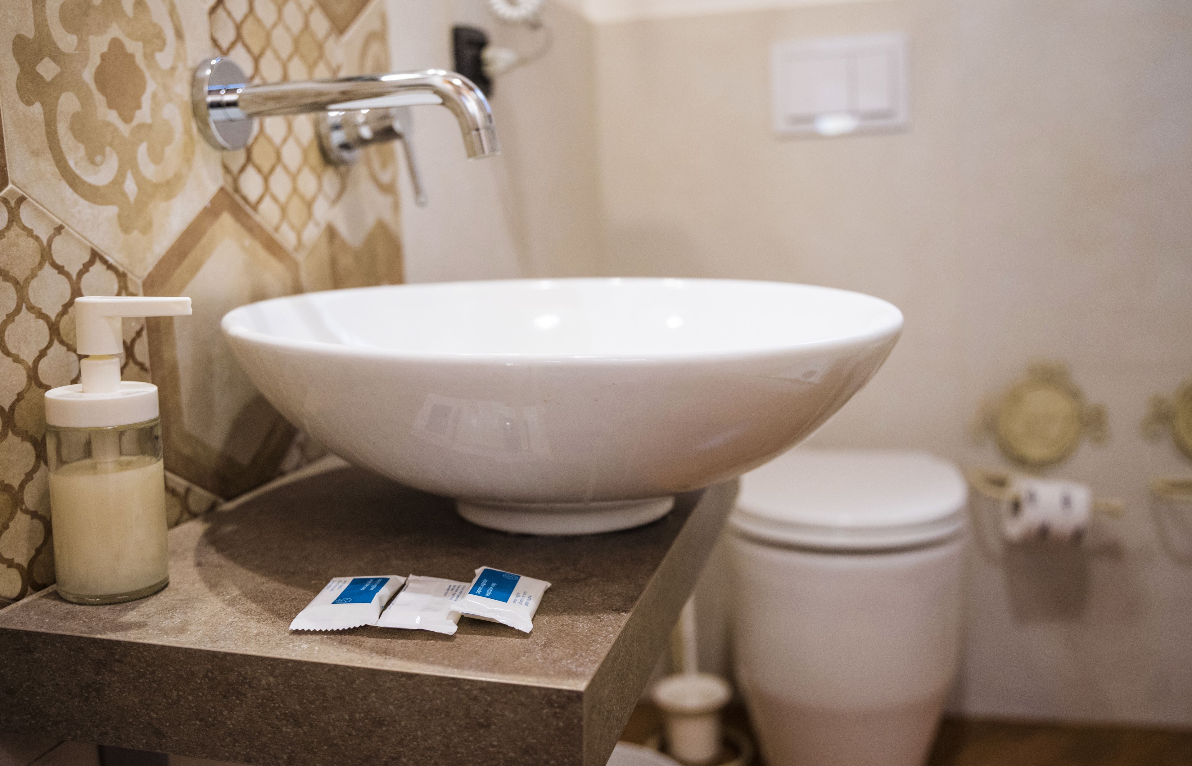 A bathroom with a large white sink, a bottle of hand soap, and two packets of lotion.