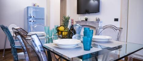 Un coin repas avec une table en verre, des chaises transparentes et un réfrigérateur bleu en arrière-plan.