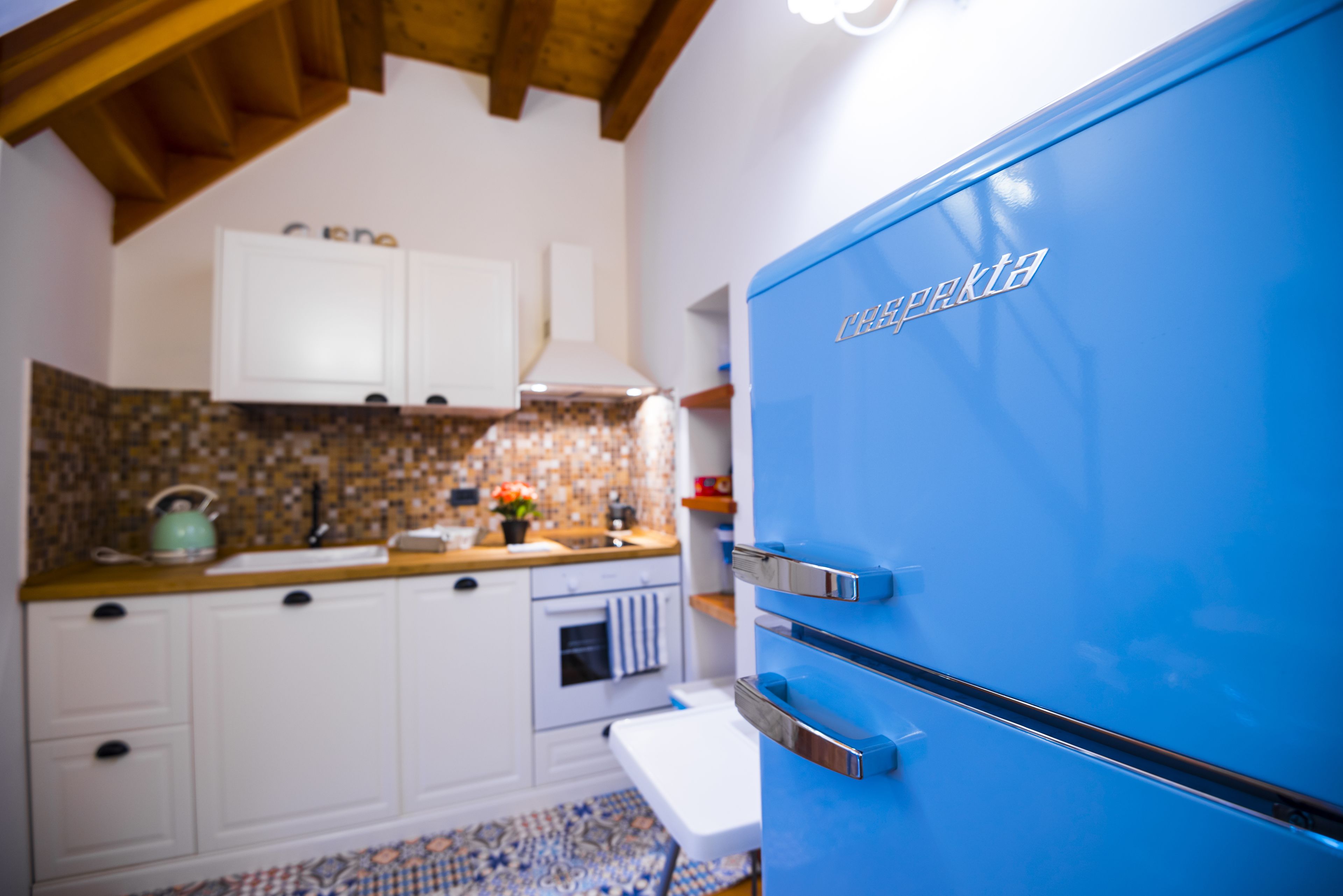 Een keuken met witte kastjes, een blauwe koelkast en een betegelde spatwand.