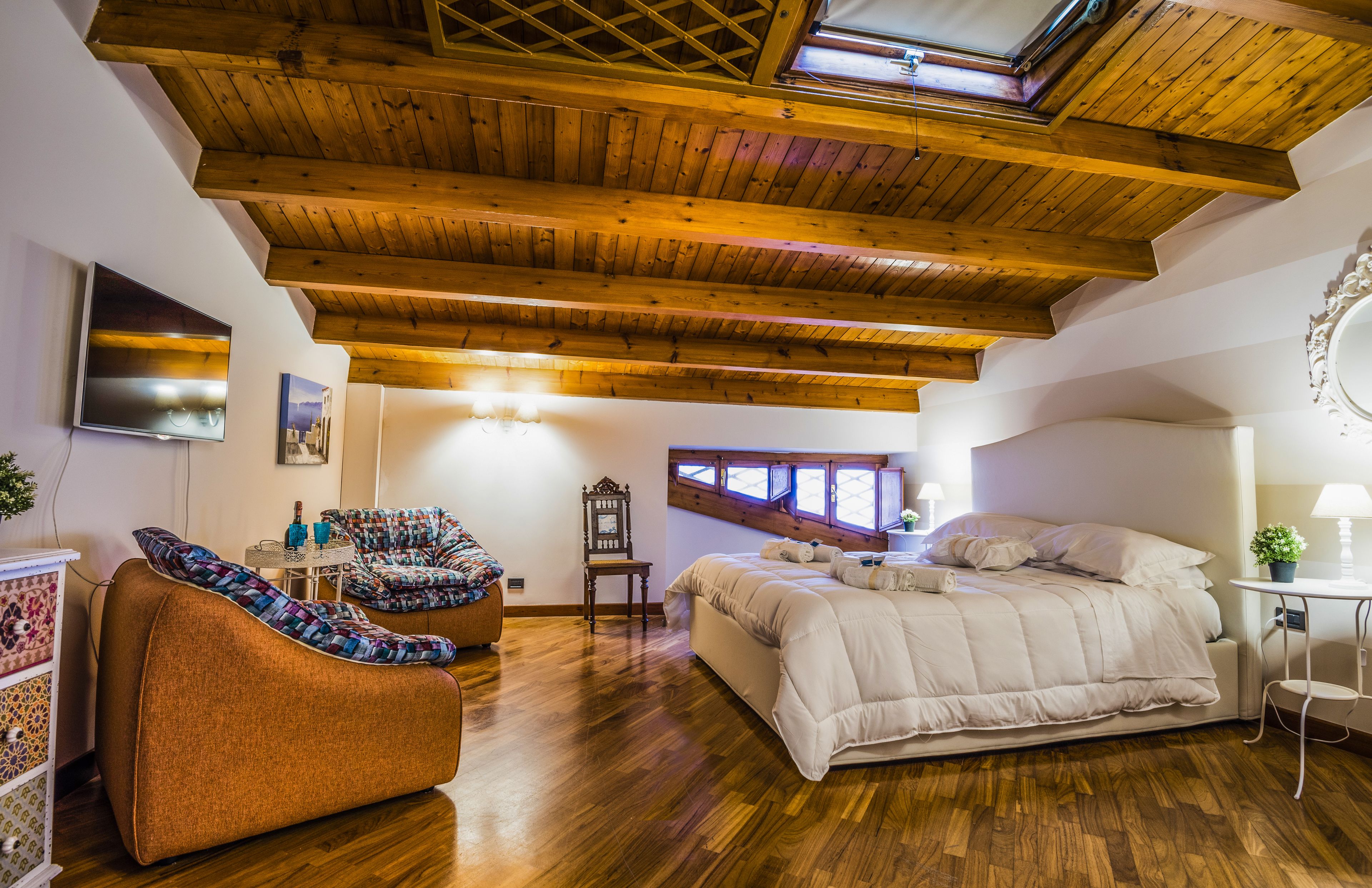 Un dormitorio con techo de madera, cama, sofá, televisor y ventana.