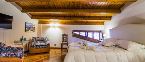 A bedroom with a wooden ceiling, a large bed, a sofa, a TV, and a window.