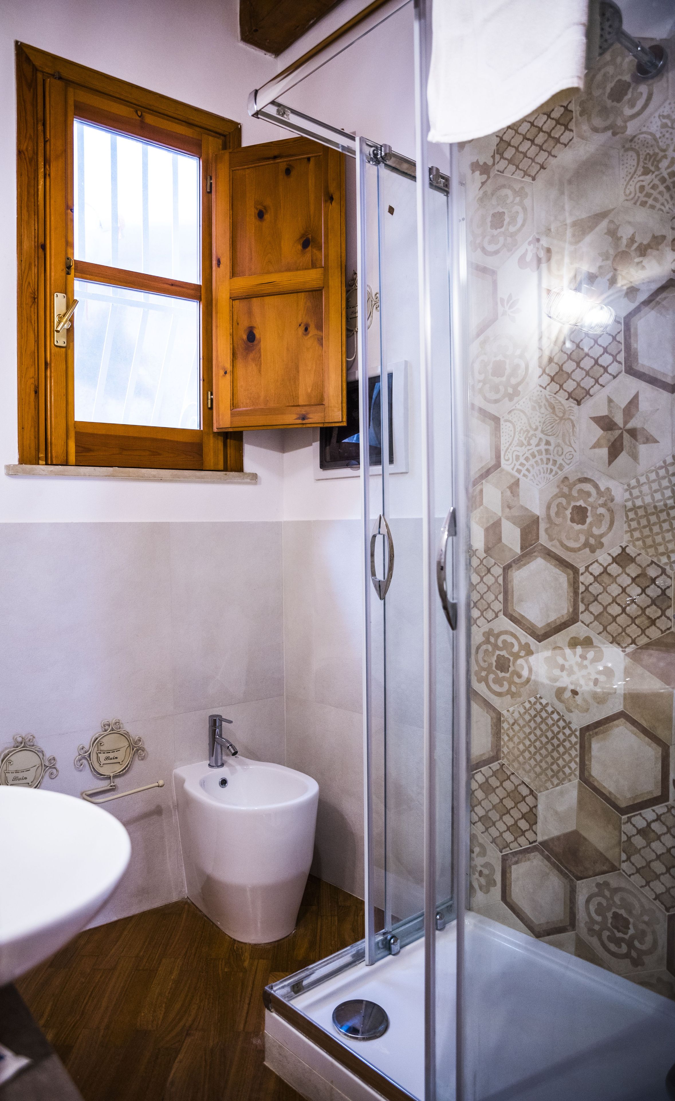 A bathroom with a shower, a bidet, a sink, and a window with wooden shutters.