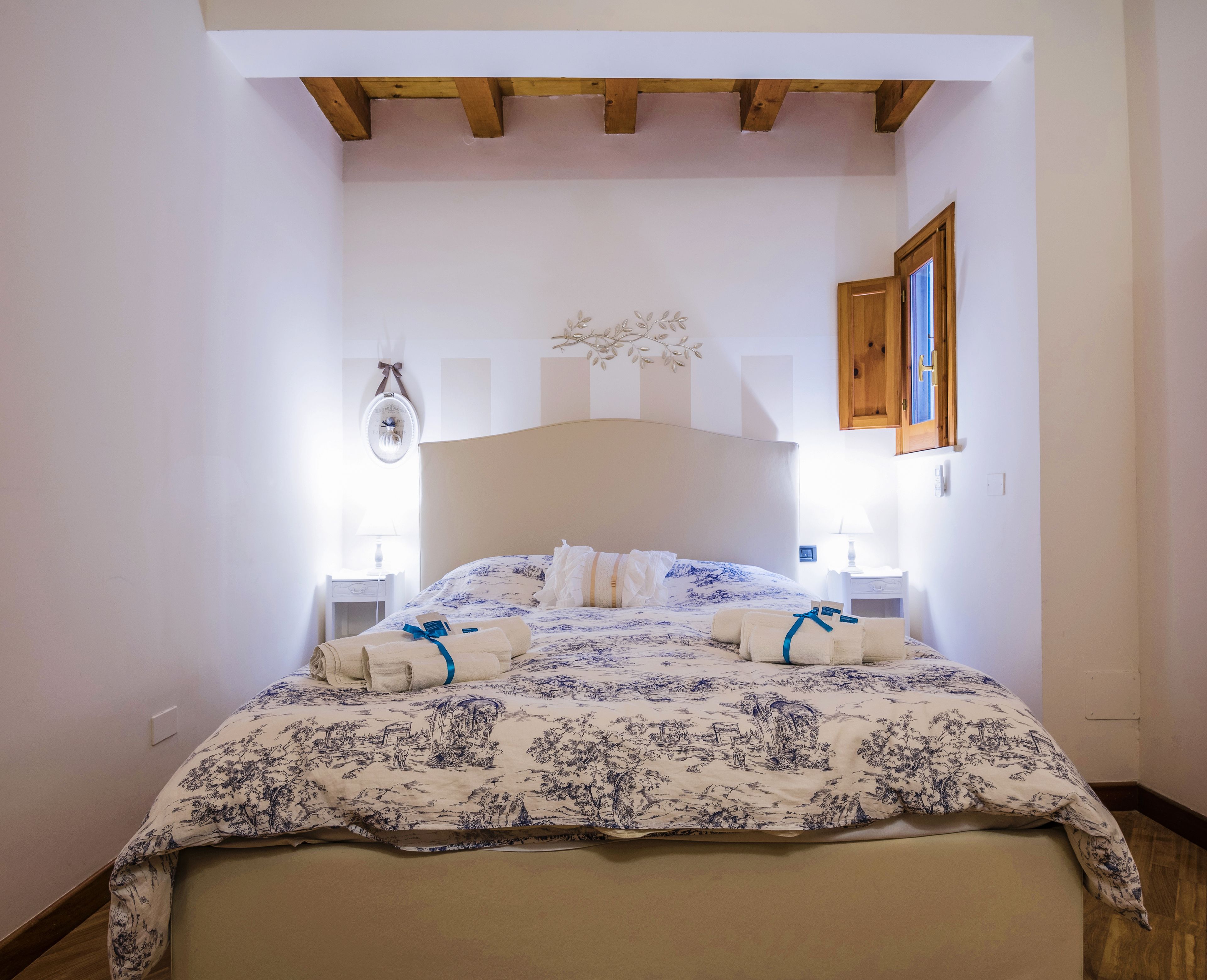 Une chambre à coucher avec un lit, des poutres en bois, une table de chevet, une lampe et un élément décoratif fixé au mur.