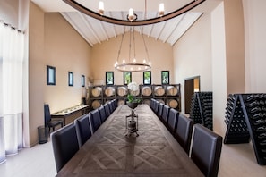 A long dining table with black leather chairs, a central floral arrangement, and wooden barrel storage in the background.