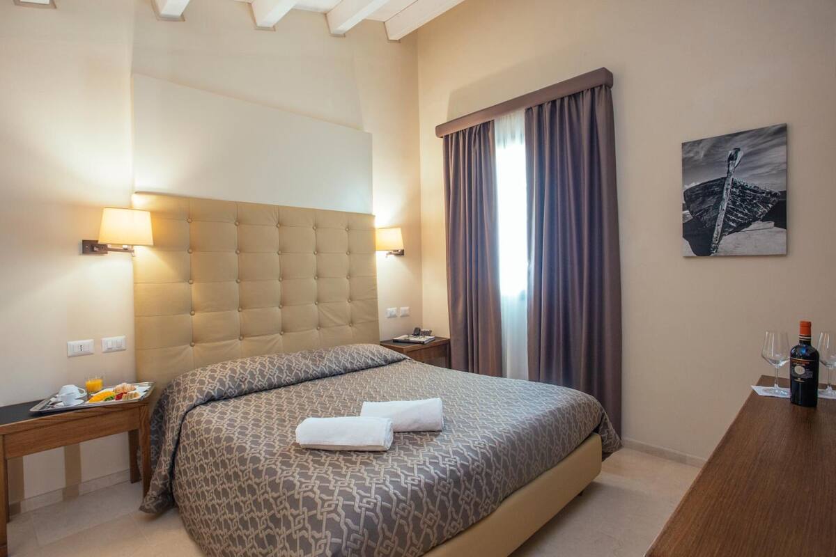 Una camera d'albergo con un letto grande, un comodino con una lampada, un vassoio con prodotti per la colazione e un quadro appeso al muro.