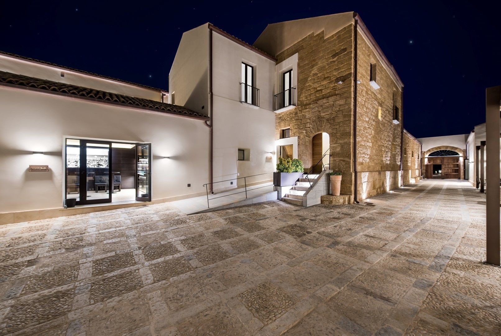 A courtyard with stone flooring, a bar area, and a staircase leading to a second floor.