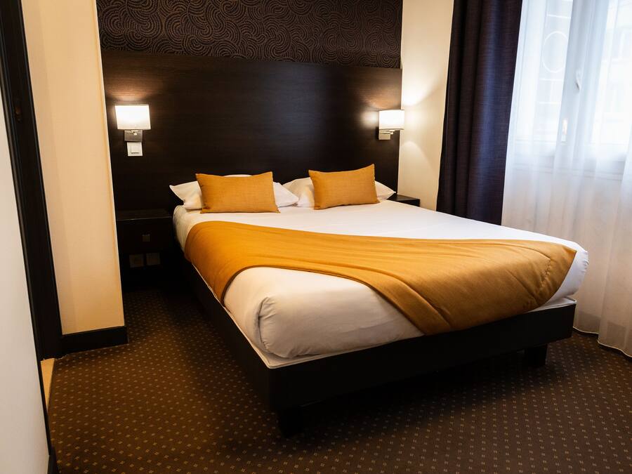 Habitación de hotel con una cama grande, dos lámparas de noche, un cabecero oscuro y una alfombra estampada.