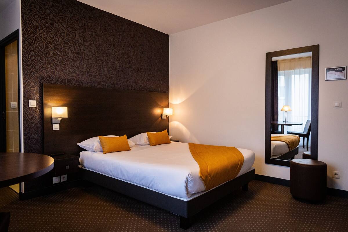 A hotel room with a large bed, two bedside lamps, a round table, and a mirror on the wall.