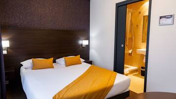 Habitación de hotel con una cama grande, dos lámparas de noche, un cabecero de madera y un baño visible a través de una puerta abierta.