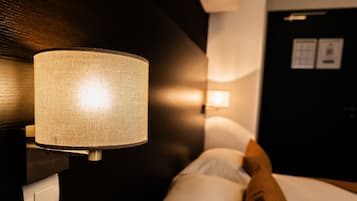 A hotel room with a bed, a wall-mounted lamp, and a door with a sign.