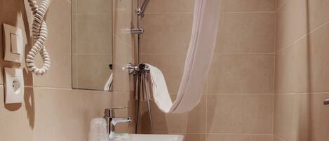 A modern bathroom with a shower, a sink, and a hairdryer mounted on the wall.