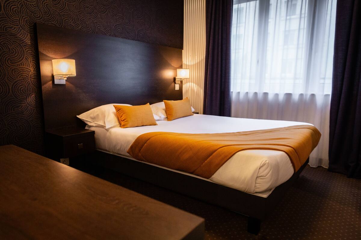 A hotel room with a large bed, two bedside lamps, a nightstand, and a wooden bench.