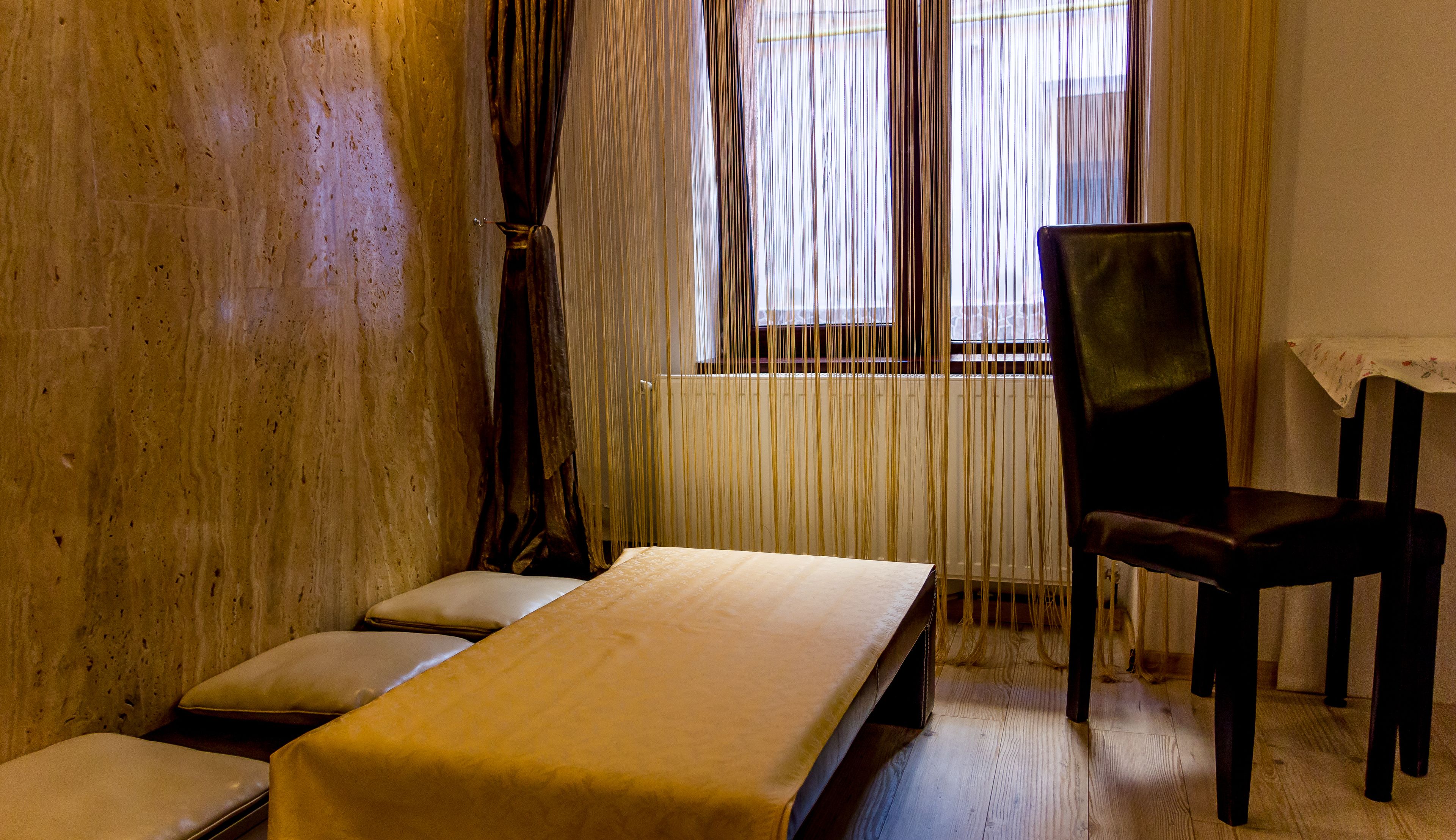 Una habitación con piso de madera, una cama con colchón blanco, una silla y un ventanal con cortinas.