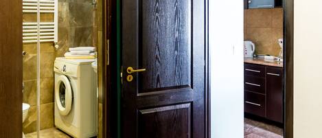 A dark wooden door with a brass handle, leading to a bathroom with a washing machine and a towel rack.