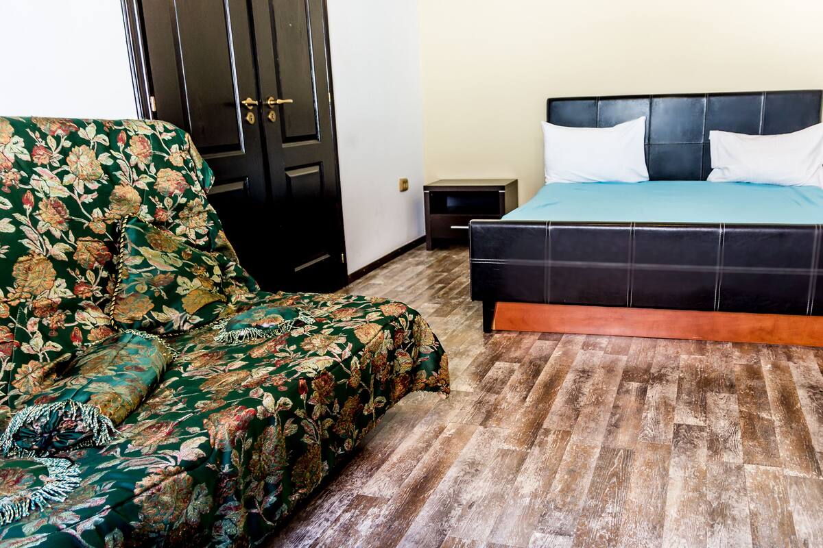 A room with a bed, a floral armchair, and a wooden floor.