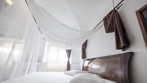 Et hotelværelse med en seng, hvide gardiner og en træsenggavl.