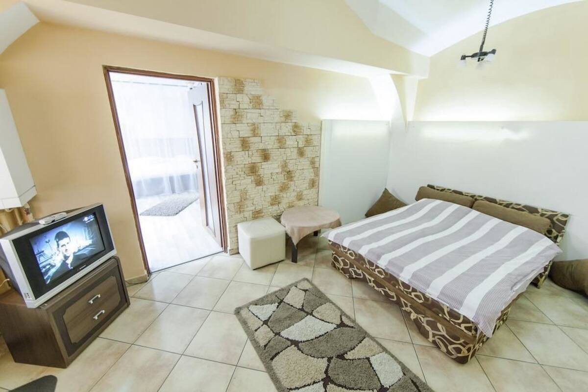 A bedroom with a bed, a television, a small table, and a wall with a stone-like texture.