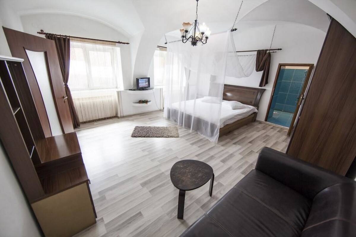 A bedroom with a bed, a sofa, a TV, and a chandelier.