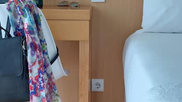 Een hotelkamer met een houten bureau, een stoel, een bed met witte beddengoed en een kleurrijk kleedje over de stoel.