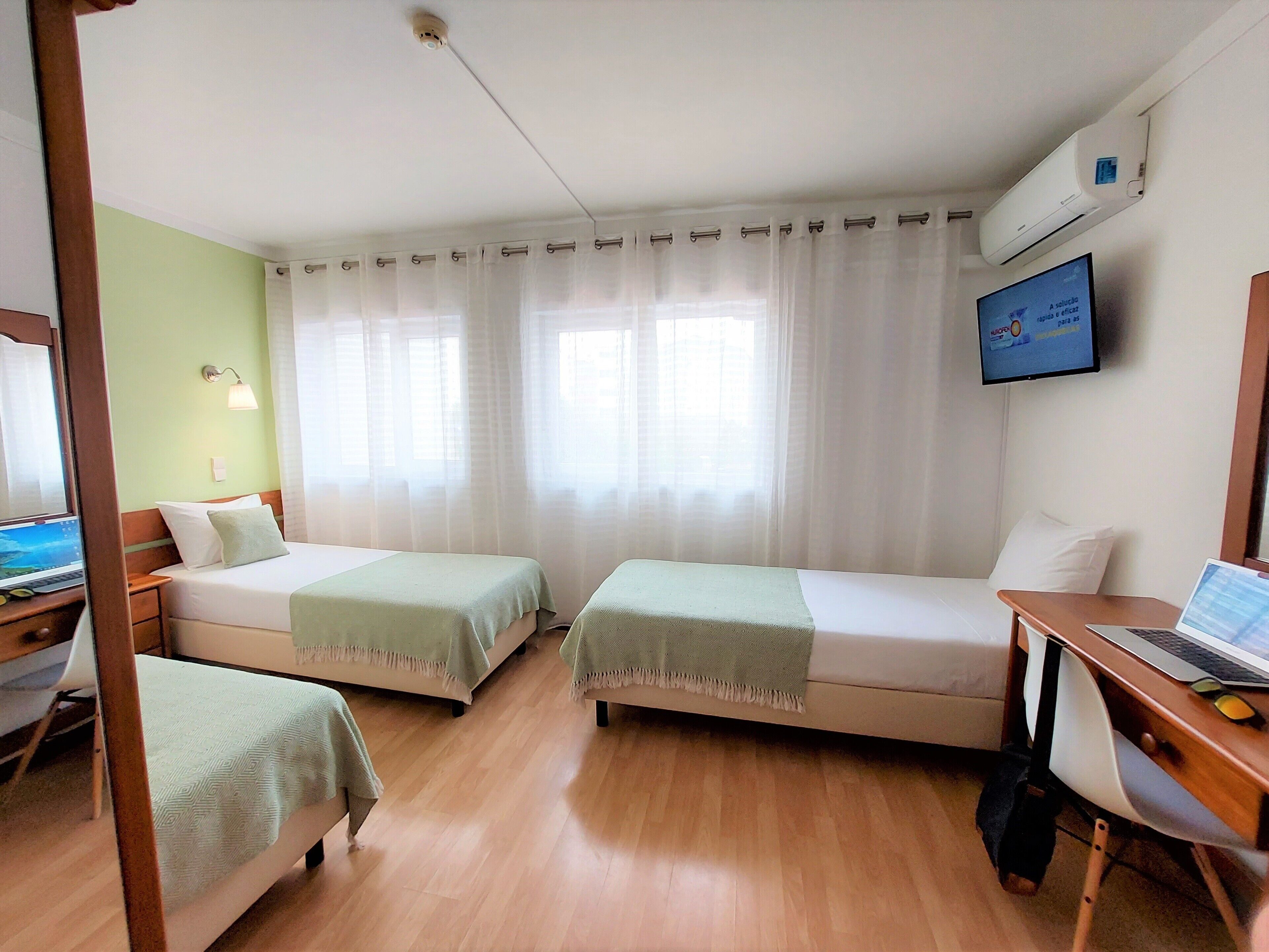 A hotel room with two beds, a desk with a laptop, a TV, and an air conditioner.