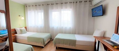 A hotel room with two beds, a desk with a laptop, a TV, and an air conditioner.