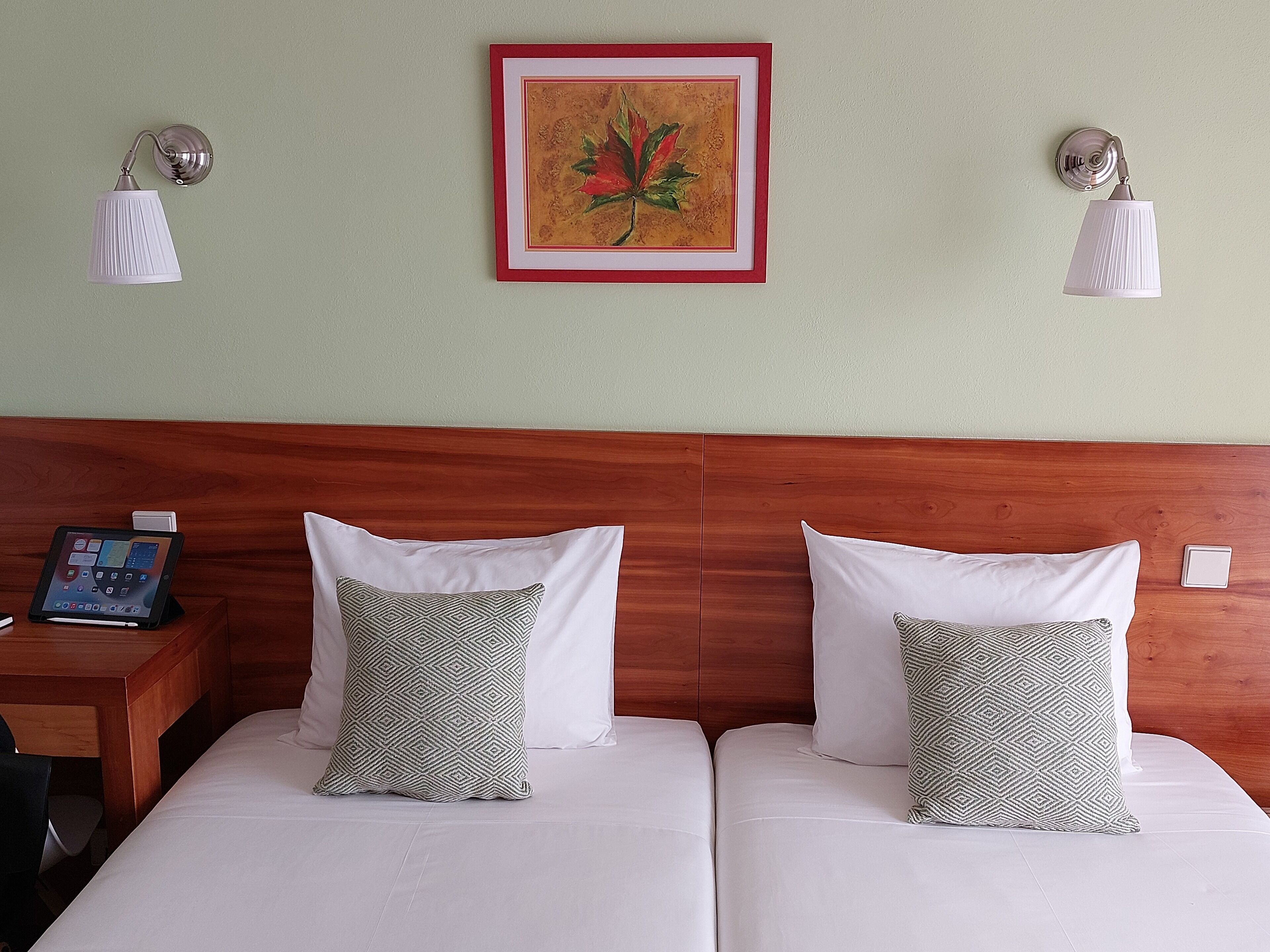 Ein Hotelzimmer mit zwei Betten, einem Holzkopfteil, einem Nachttisch mit Telefon und einem gerahmten Kunstwerk an der Wand.