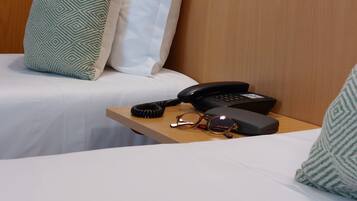 Une chambre d’hôtel avec un lit, des oreillers, une table de chevet avec un téléphone, des verres et une valise.