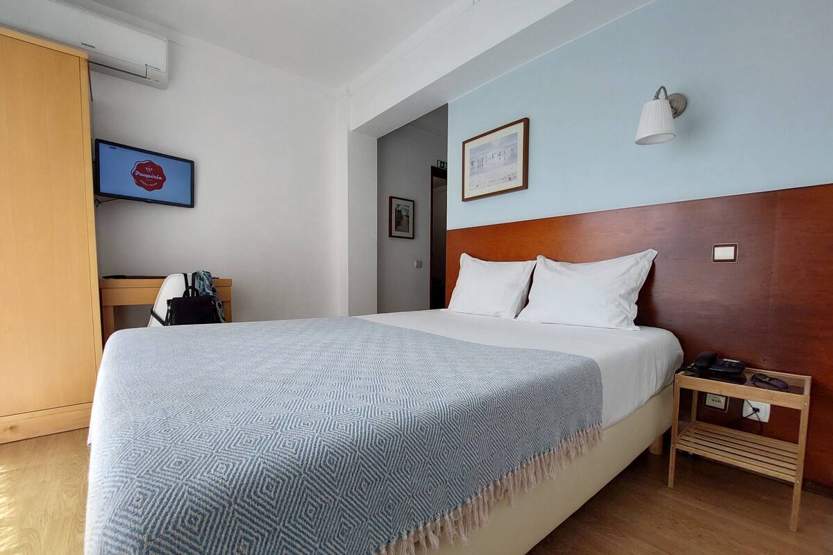 A hotel room with a bed, a nightstand, a lamp, a wardrobe, and a wall-mounted air conditioner.