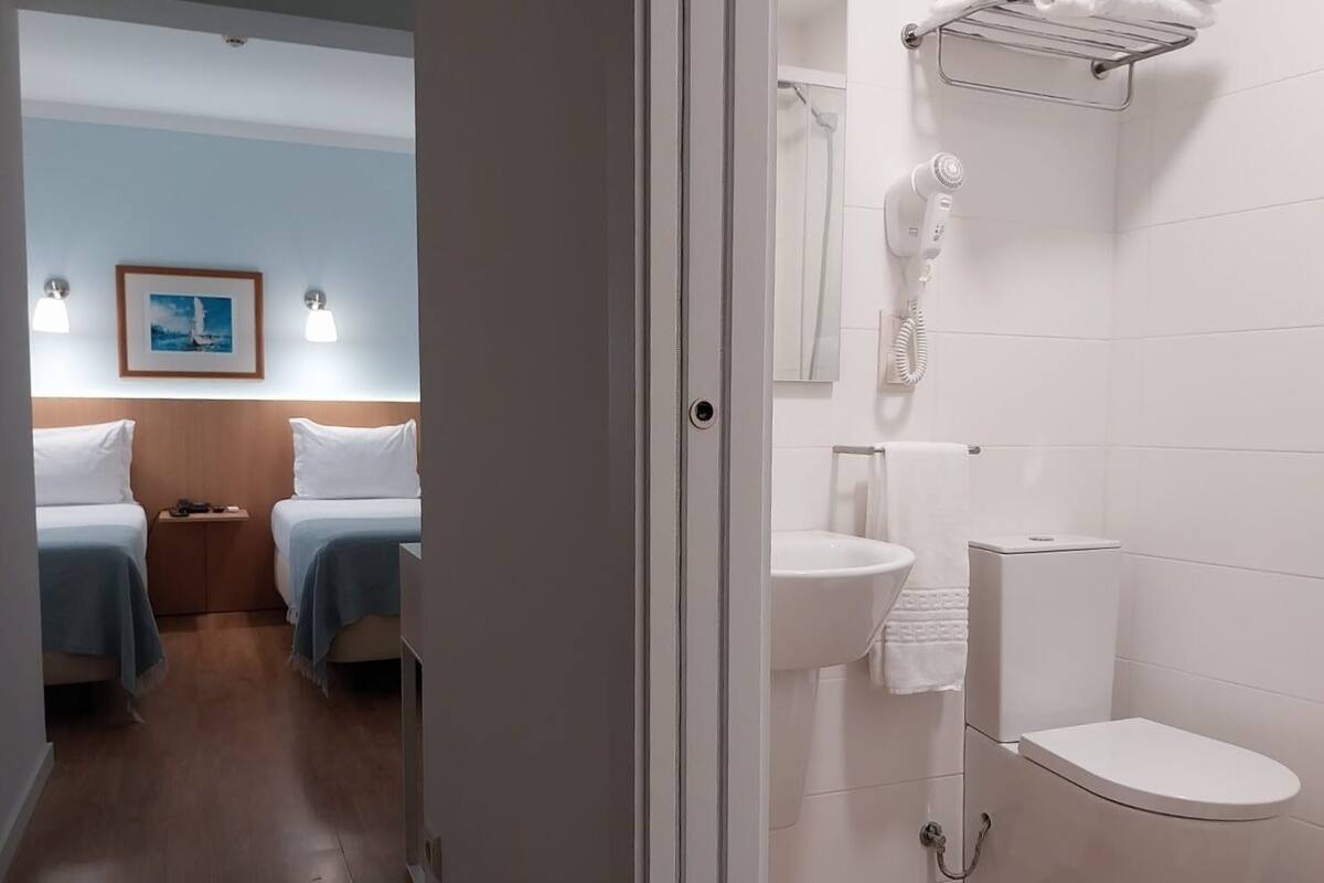 A hotel room with two beds, a bathroom with a sink and toilet, and a shower area.