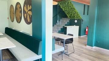 Un intérieur moderne avec des murs de couleur turquoise, un comptoir d’accueil, un escalier et un espace détente avec des tables et des chaises.