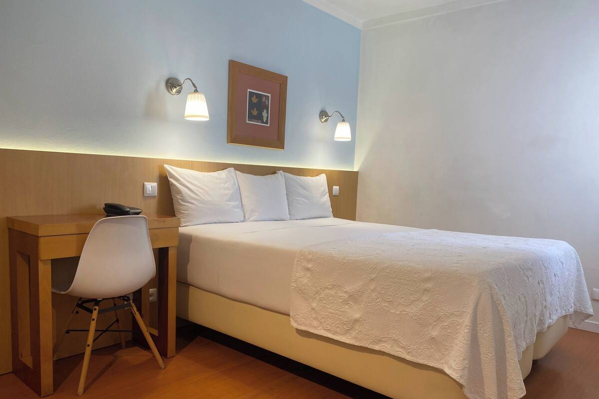 A neatly arranged hotel room with a bed, bedside table, chair, and two wall-mounted lamps.