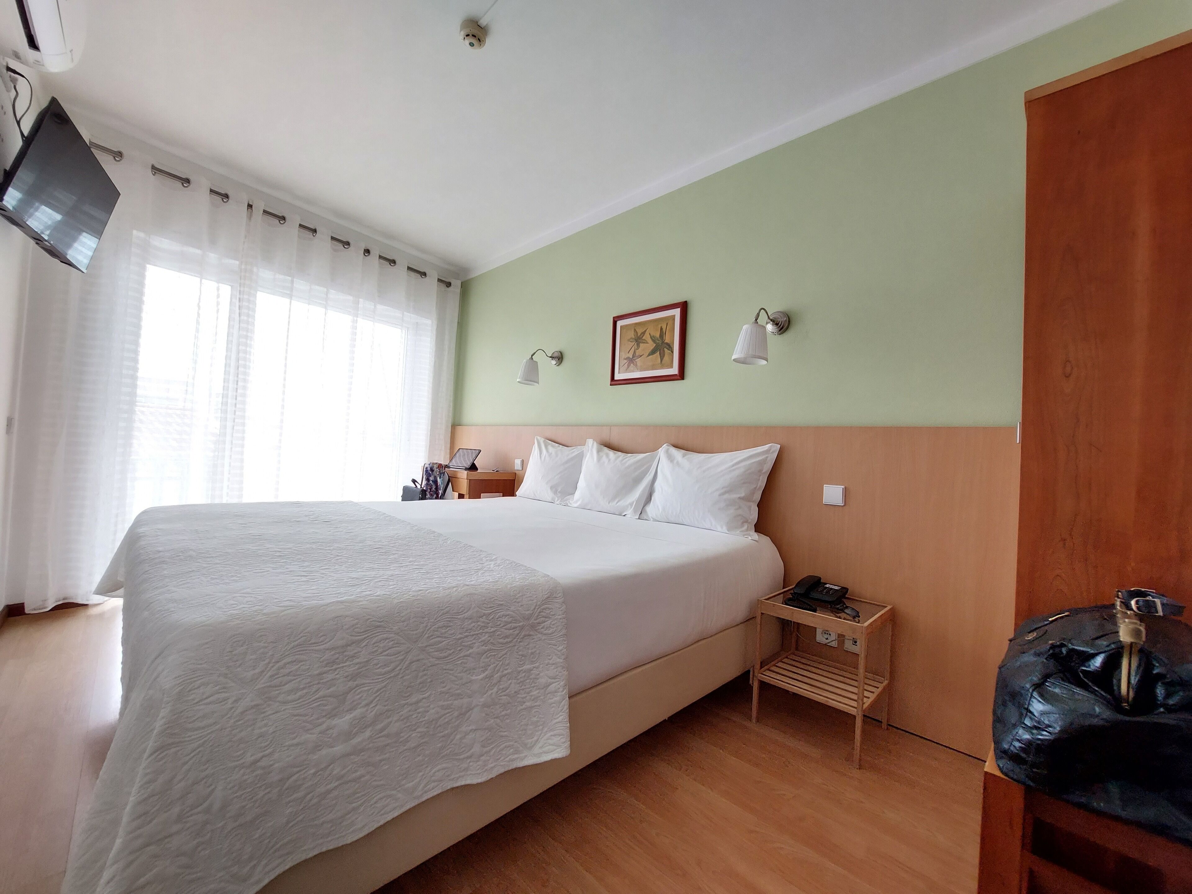 Een hotelkamer met een groot bed, een bureau met een laptop, een telefoon en een wandlamp.