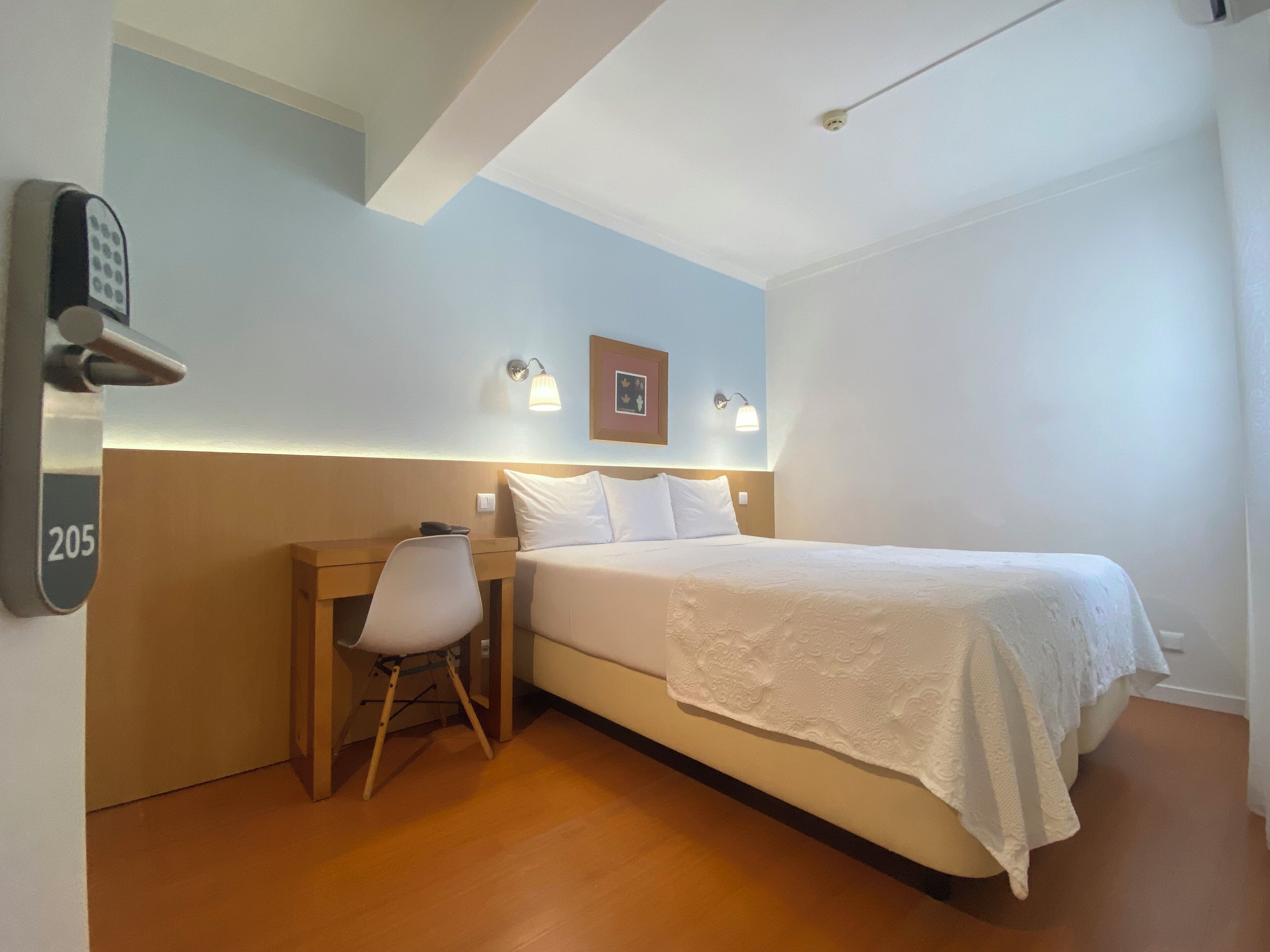 Ein Hotelzimmer mit Bett, Schreibtisch, Stuhl und einem an der Wand befestigten Telefon.