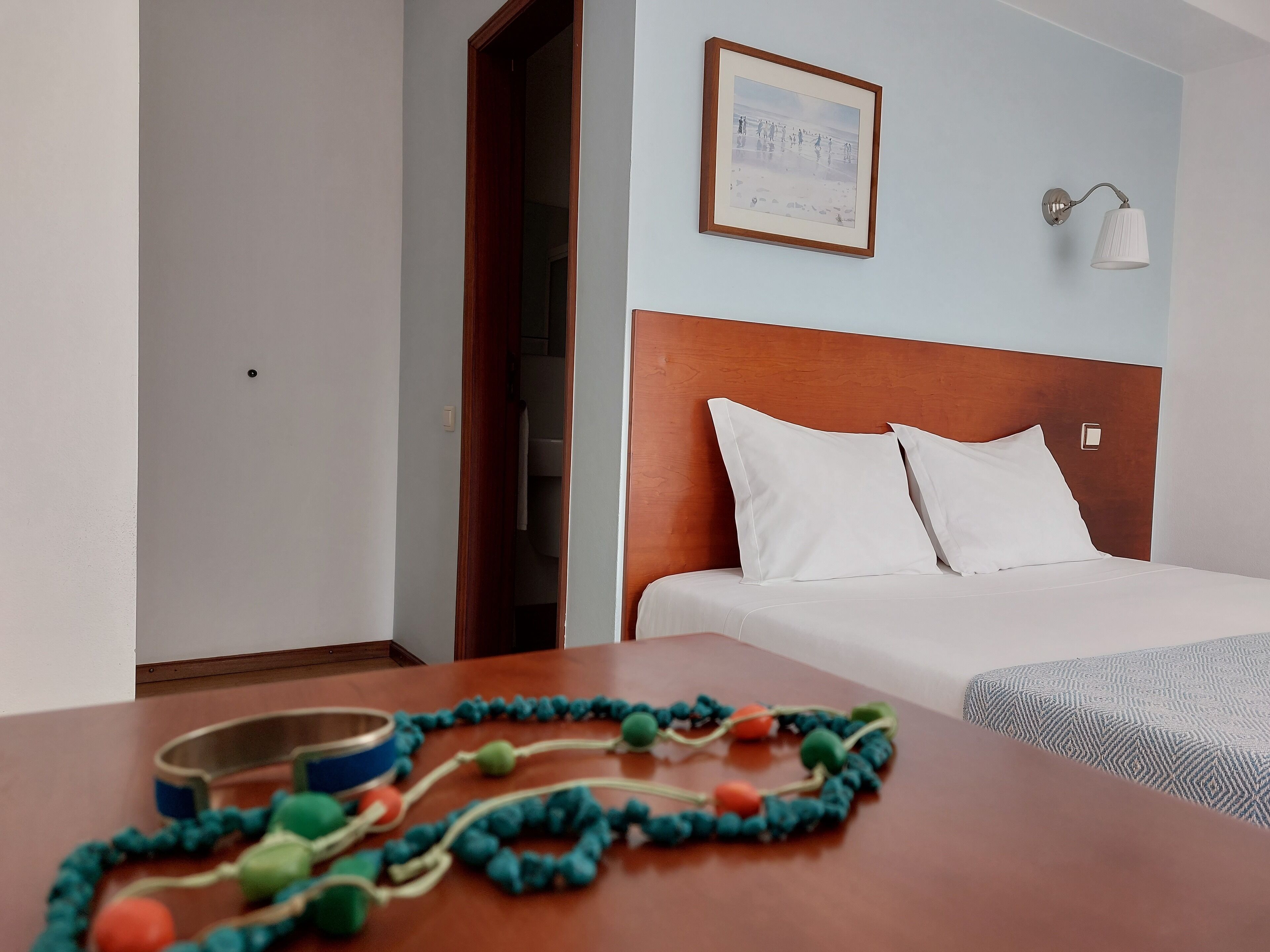 Habitación de hotel con una cama, cabecera de madera, un cuadro en la pared y una lámpara.