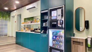 Una kitchenette con un refrigerador lleno de bebidas, una cafetera y un dispensador de jugo.