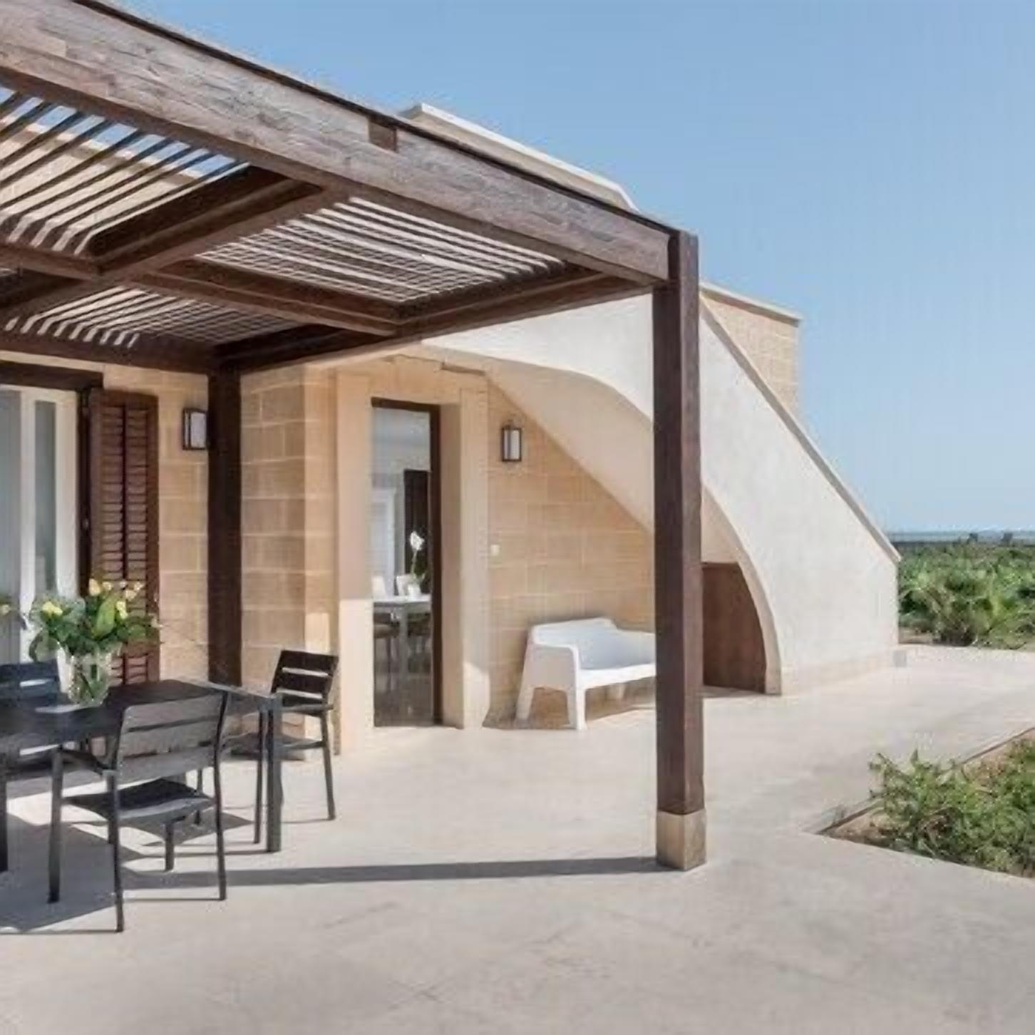 A modern outdoor patio with a wooden pergola, a table with chairs, and a white lounge chair.