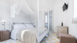 Een moderne slaapkamer met een bed, nachtkastjes, een televisie en een klein tafeltje met glazen en een fles.
