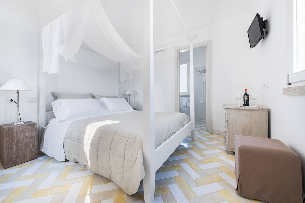 Ein modernes Schlafzimmer mit einem Bett, Nachttischen, einem Fernseher und einem kleinen Tisch mit Gläsern und einer Flasche.