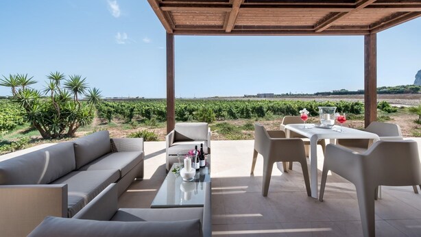 Een terras met een pergola, een bank, stoelen en een tafel met drankjes.
