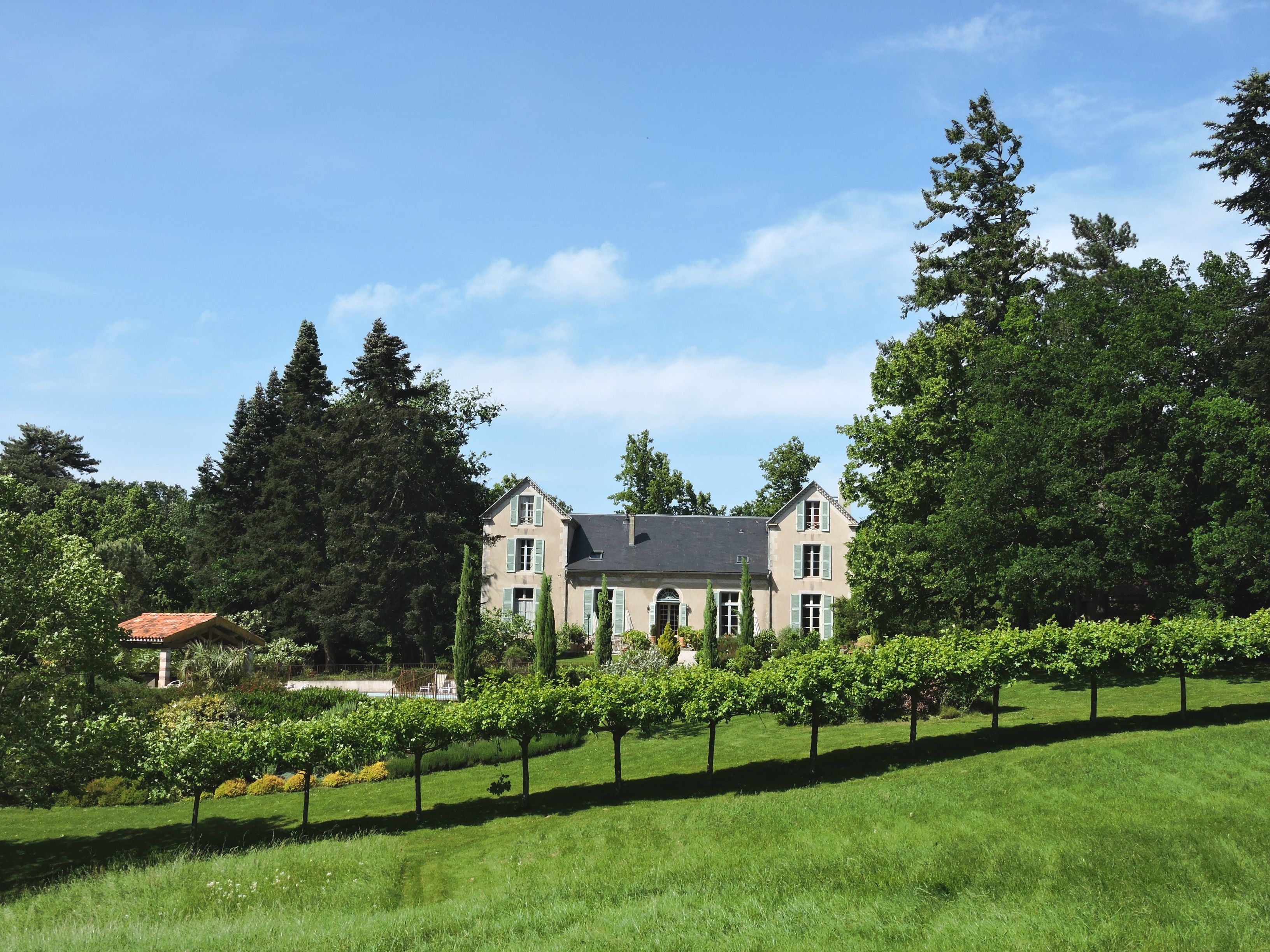 A large, two-story house with a sloped roof, surrounded by a well-maintained garden and trees.