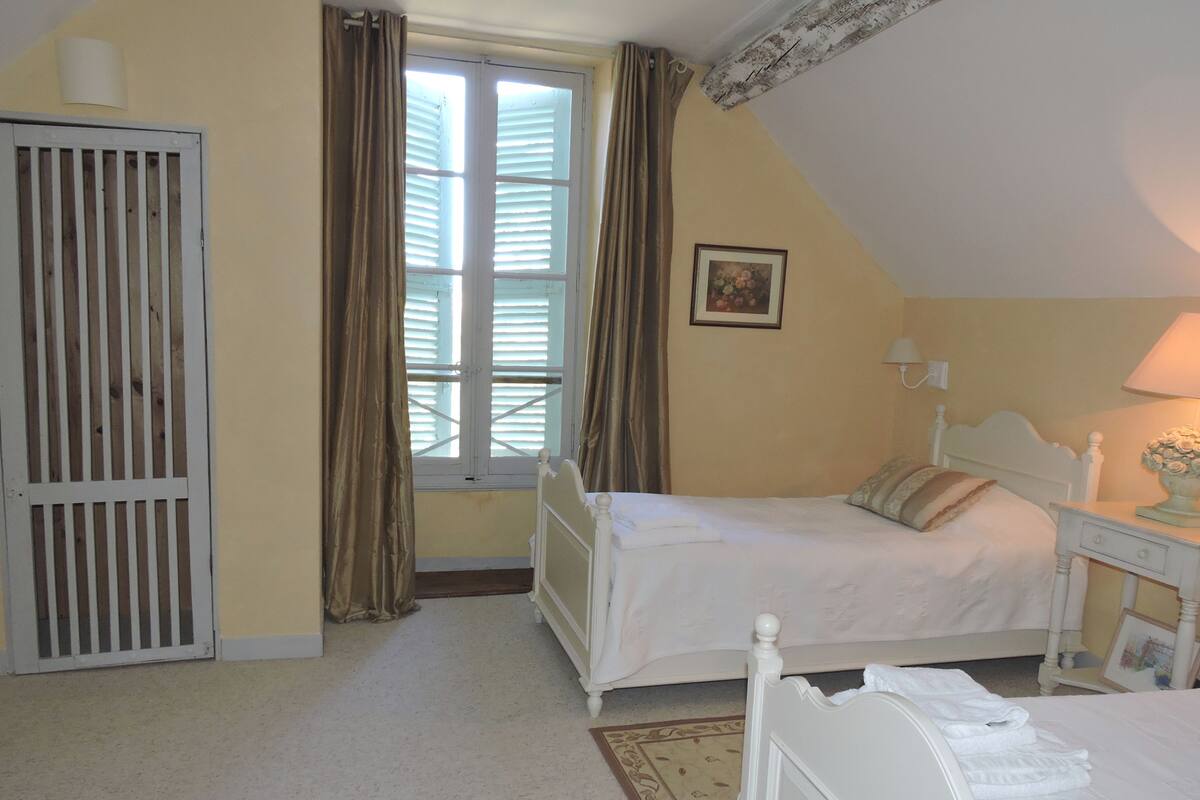 Un dormitorio con cama, mesita de noche, lámpara, ventana con cortinas y puerta con reja de metal.
